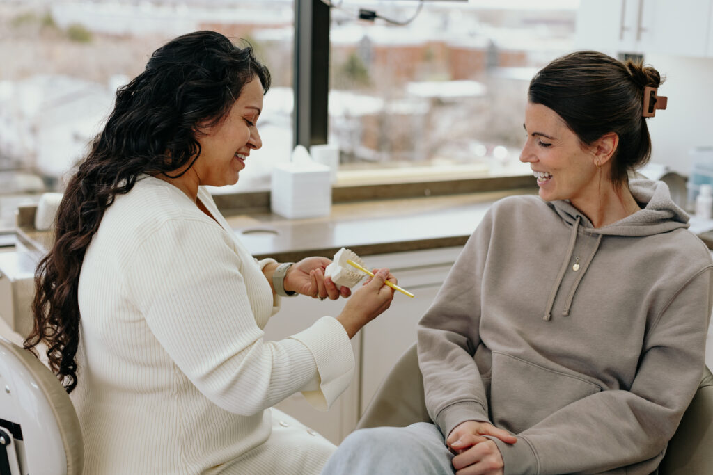 Dental hygienist vs dentist: hygienist showing a patient a tooth model during a preventive visit at a Denver biological dental practice